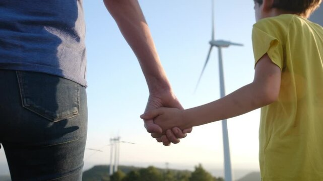 Wind turbine power plant backdrop framing mother and son holding hands, symbolizing renewable energy commitment and environmental legacy