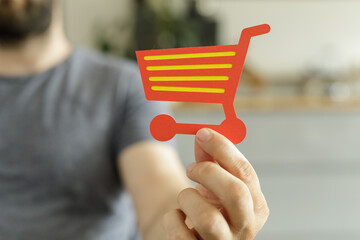 Close-up of a man holding a red paper shopping cart icon.  Ecommerce, online shopping, retail...