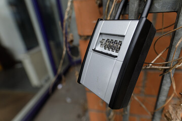 Close-up of a silver combination lockbox attached to a brick wall outdoors.  Security and safety concept.