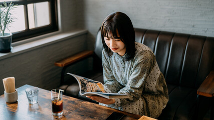 カフェのソファに座って雑誌を読む若い女性