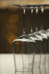Upturned empty clean glasses on mirror surface against blurred background, closeup. Bokeh effect