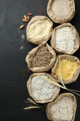Different types of flour in paper bags on black table, flat lay