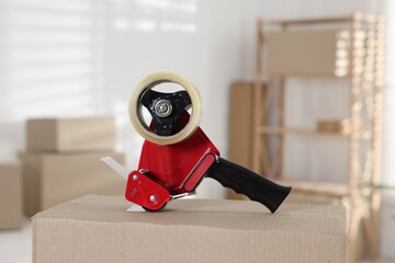 Dispenser with adhesive tape on cardboard box indoors, closeup