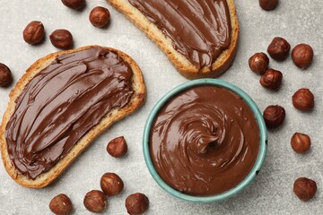 Toasts with tasty chocolate hazelnut spread and nuts on grey table, flat lay