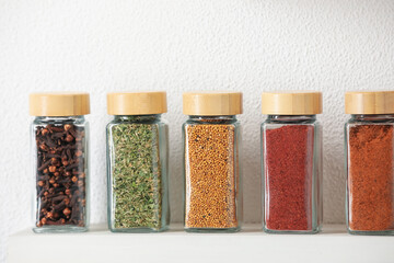 Different aromatic spices in jars on white shelf indoors, closeup