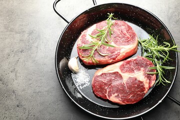 Pieces of raw beef meat and spices in baking dish on gray textured table, top view