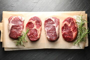 Pieces of raw beef meat, rosemary and salt on black table, top view
