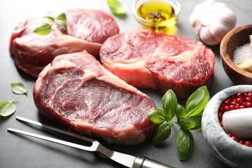 Pieces of raw beef meat, spices and carving fork on grey table, closeup