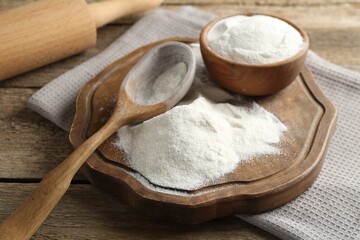 Wheat flour, spoon and rolling pin on wooden table, closeup