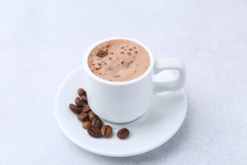 Aromatic coffee in cup, beans and saucer on light table, closeup