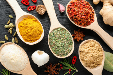 Different aromatic spices in spoons on black table, closeup