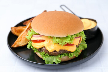 Tasty cheeseburger with sauce and potato wedges on white table, closeup