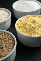 Different types of flour in bowls on black table, closeup