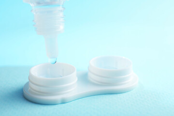 Dripping solution into case with contact lenses on light blue background, closeup