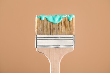Brush with turquoise paint on light brown background, closeup