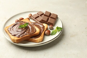 Toasts with tasty chocolate spread, pieces, mint and hazelnuts on light table, closeup
