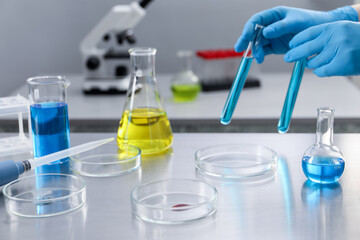 Scientist holding test tubes at table with Petri dishes in laboratory, closeup