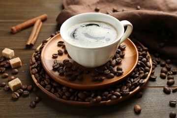 Aromatic coffee in cup, beans, brown sugar and cinnamon on wooden table, closeup