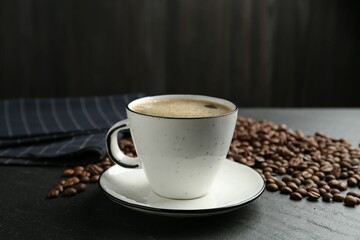 Aromatic coffee in cup and beans on black table, closeup