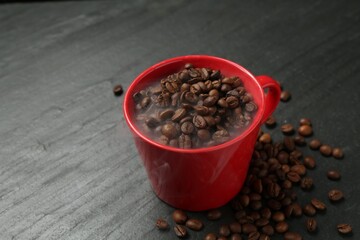 Aromatic coffee beans in cup on black table, closeup. Space for text