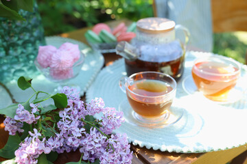 Beautiful lilac flowers, sweets and tea on wooden table in garden, closeup