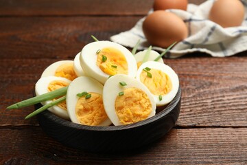 Halves of hard boiled eggs with green onions on wooden table, closeup