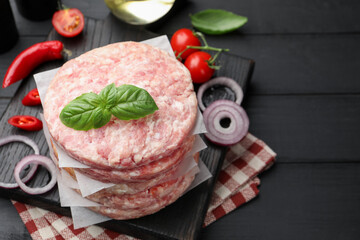 Fresh raw patties for burger, spices and tomatoes on black wooden table, above view. Space for text