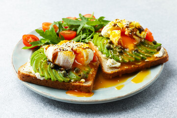 Delicious sandwiches with avocado, poached egg, salmon, tomatoes and arugula on gray table, closeup