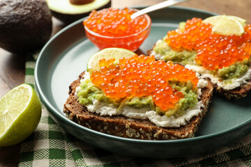 Delicious sandwiches with avocado, red caviar, cream cheese and lime on table, closeup