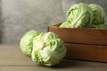 Fresh whole cabbages and crate on wooden table, closeup