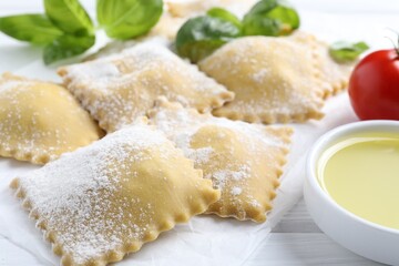 Uncooked ravioli, basil, tomatoes and oil on white wooden table, closeup