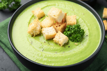 Tasty pea cream soup with croutons and broccoli served on black table, closeup