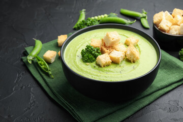 Tasty pea cream soup with croutons and broccoli served on black table, closeup
