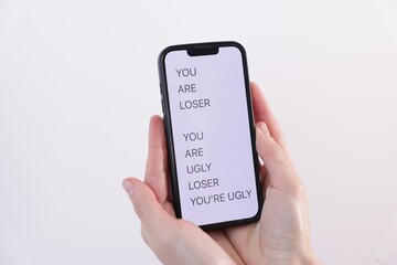 Cyber bullying. Woman holding smartphone with insults on light background, closeup