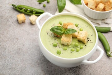 Tasty pea cream soup with croutons and basil served on grey table, closeup