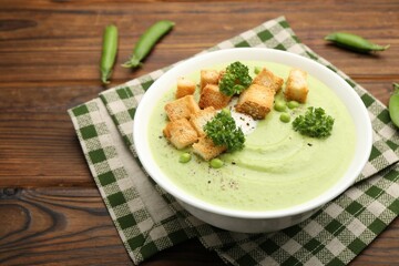 Tasty pea cream soup with croutons and broccoli served on wooden table, closeup