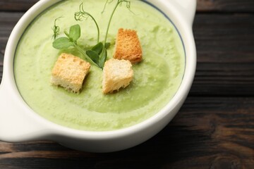 Tasty pea cream soup with croutons and microgreens on dark wooden table, closeup