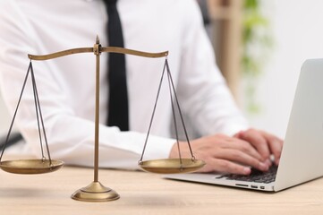 Judge working with laptop and scales on desk indoors, selective focus