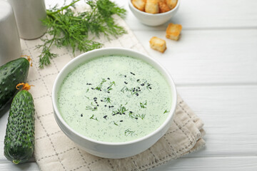 Tasty cucumber soup, croutons and ingredients on white wooden table, closeup