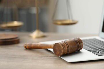 Laptop, judge's gavel and scales on wooden table in office, closeup