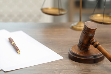 Papers, judge's gavel and scales on wooden table in office, closeup
