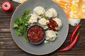 Tasty khinkali with spices, sauce and cilantro on wooden table, flat lay
