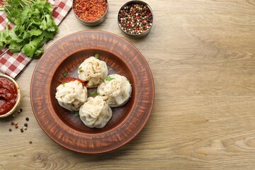 Tasty khinkali with sauce and spices on wooden table, flat lay. Space for text