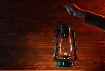 Woman holding vintage kerosene lantern near wooden wall, closeup. Space for text