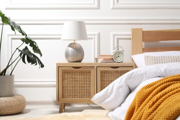 Fototapeta na wymiar Bedside table with lamp, alarm clock and books near bed indoors