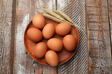 Raw eggs and spikes of wheat on wooden table, top view
