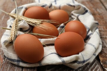 Raw eggs, fabric and spikes of wheat on wooden table, closeup