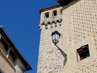 A tall stone tower rises against a clear blue sky, surrounded by charming buildings