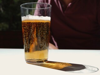 A tall glass filled with a sparkling golden drink sits on a white table in a sunny outdoor setting