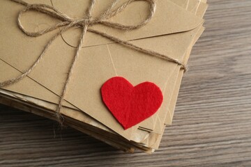 Stack of love letters and paper heart on wooden table, top view